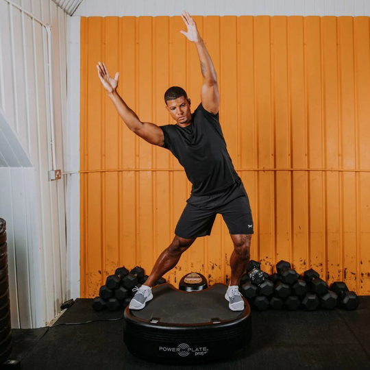 Person using a Power Plate pro5HP with dumbbells in the background