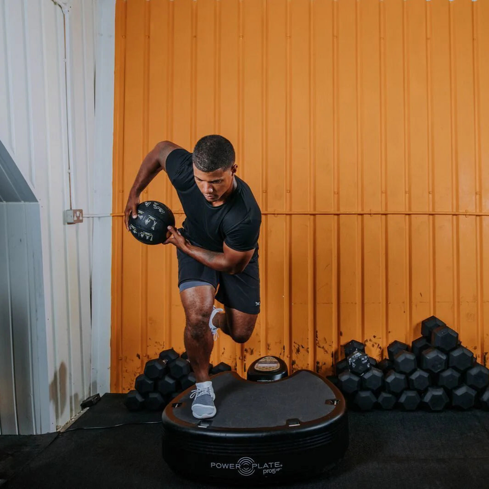 Person using a Power Plate pro5HP with dumbbells in the background