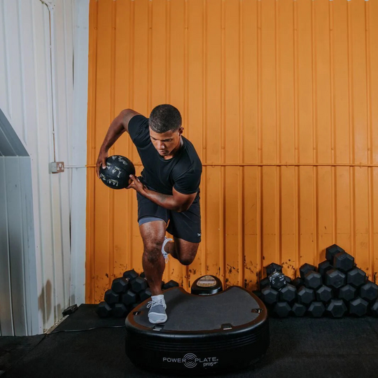 Person using a Power Plate pro5HP with dumbbells in the background
