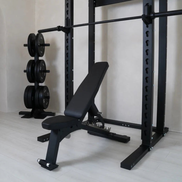 Black weight bench and squat rack in a gym setting with weights on a white floor.
